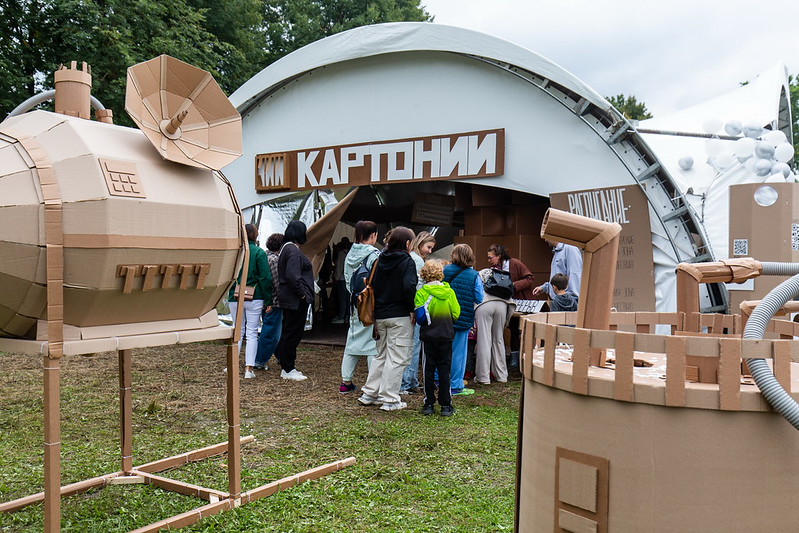 Visitors entering the Cardboardia tent past a large cardboard machine sculpture