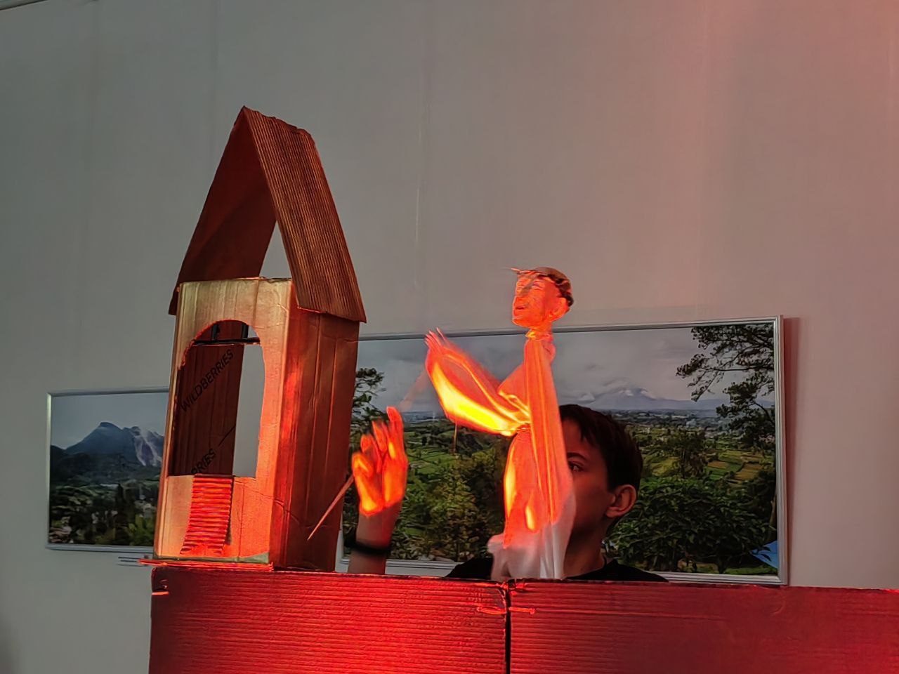 A backlit cardboard puppet performance, hands raised in a dramatic pose