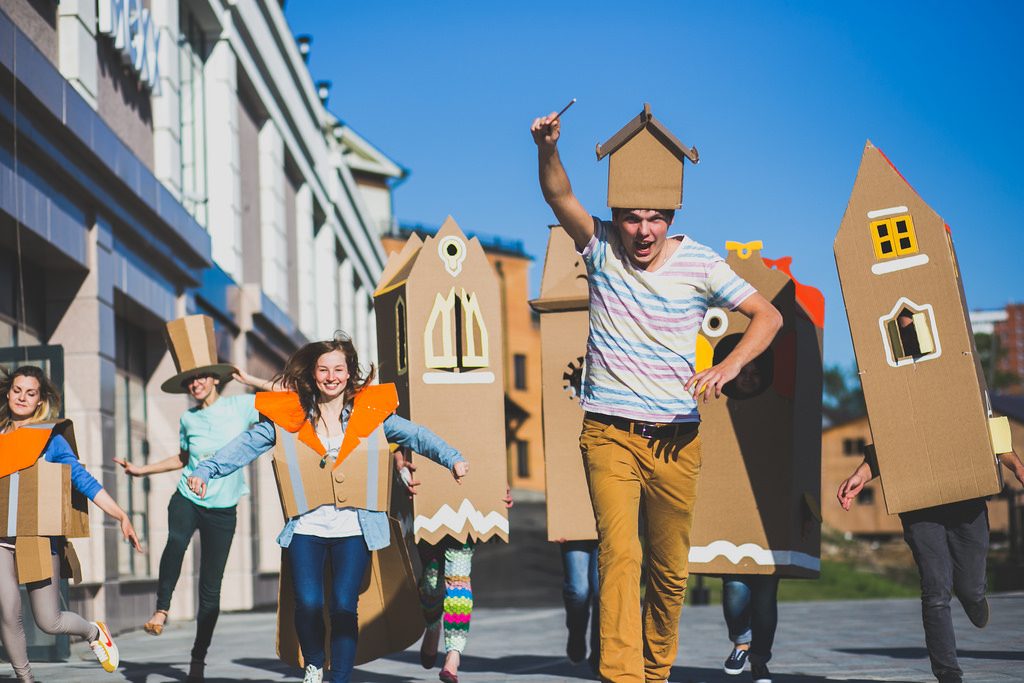 A joyful group running down a street in cardboard house costumes