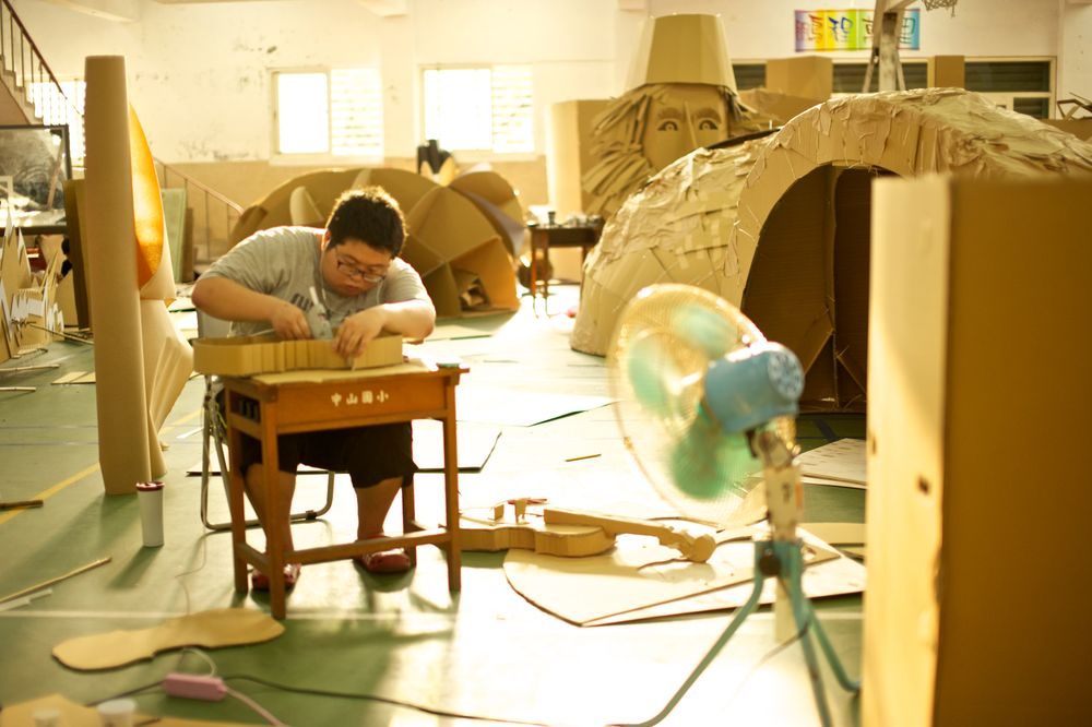 A craftsperson building a cardboard stringed instrument in a sunlit workshop