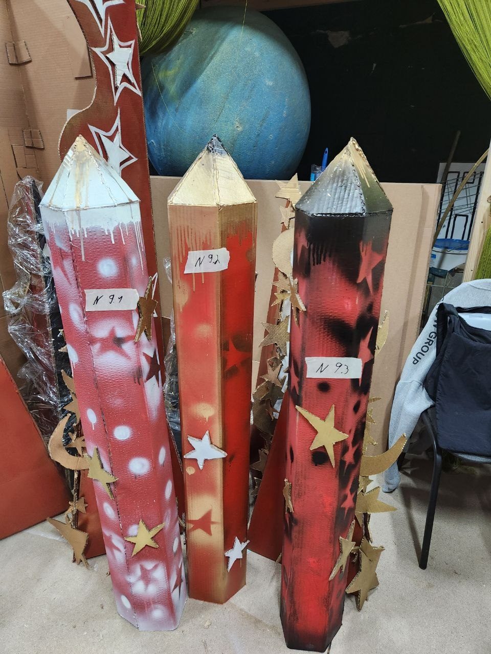Three tall cardboard rocket props painted red and gold with star decorations