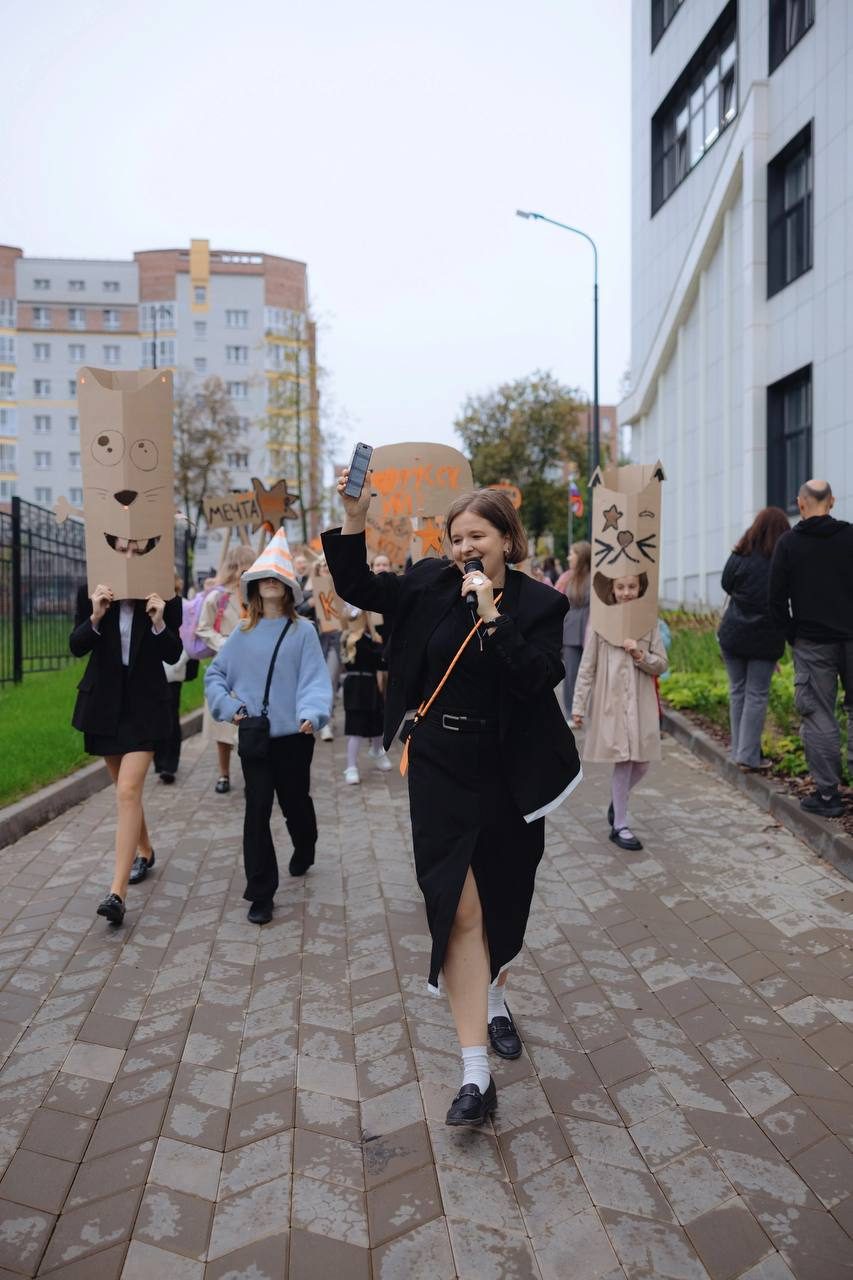 A woman leading a cardboard procession, speaking into a microphone
